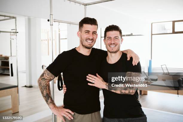 smiling male instructor with arm around man standing in pilates studio - arm tattoos for black men fotografías e imágenes de stock