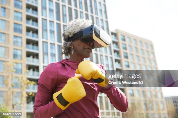 senior woman wearing virtual reality headset while exercising in park - gul handske bildbanksfoton och bilder