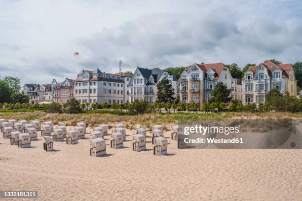 germany, mecklenburg-western pomerania, heringsdorf, hooded beach chairs on sandy beach with residential buildings in background - usedom 個照片及圖片檔