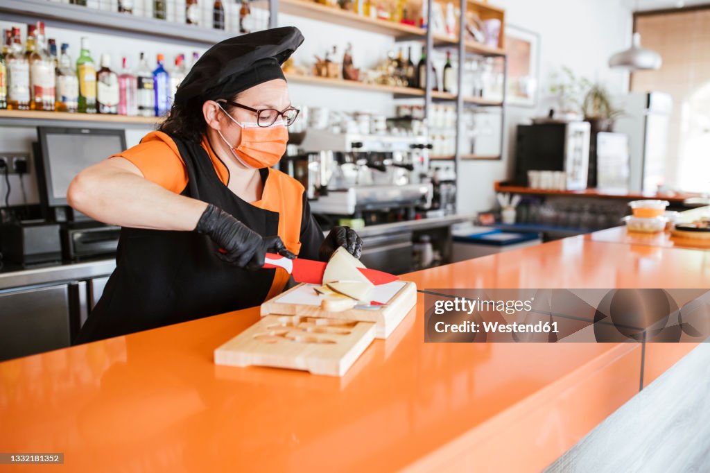 Female chef cutting manchego cheese at counter during pandemic
