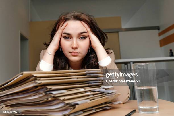 tired young businesswoman sitting with hand in hair at desk in office - european map stockfoto's en -beelden