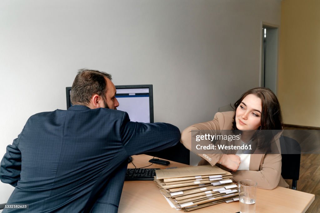 Male and female professionals greeting with elbow bump in office