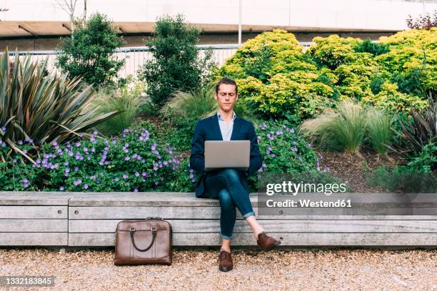 businessman using laptop while sitting on bench at park - green economy stock-fotos und bilder