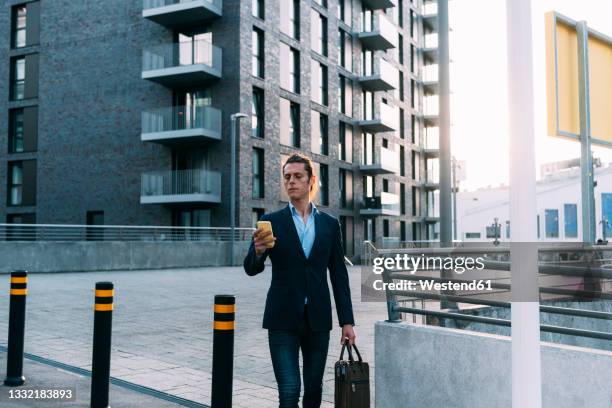 businessman with briefcase using mobile phone while walking in city - borne tactile photos et images de collection