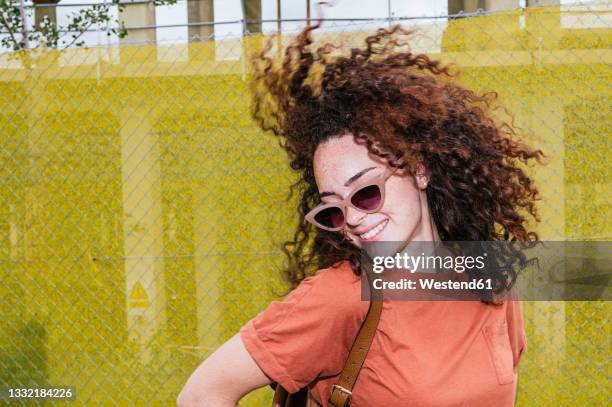 smiling young woman tossing hair in front of yellow fence - hair toss stock pictures, royalty-free photos & images