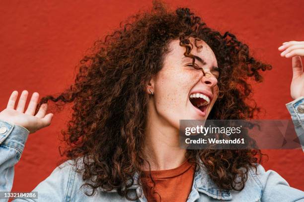 cheerful young woman with curly hair singing in front of red wall - singen stock-fotos und bilder