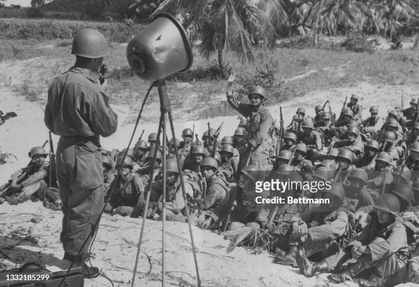 Private Luis Torregrosa, a Puerto Rican teacher in civilian life, instructs an English class at Camp Tortuguero with the aid of a microphone and a...