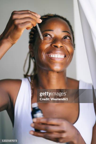 smiling afro woman looking up while applying face serum - mature woman beauty stock pictures, royalty-free photos & images