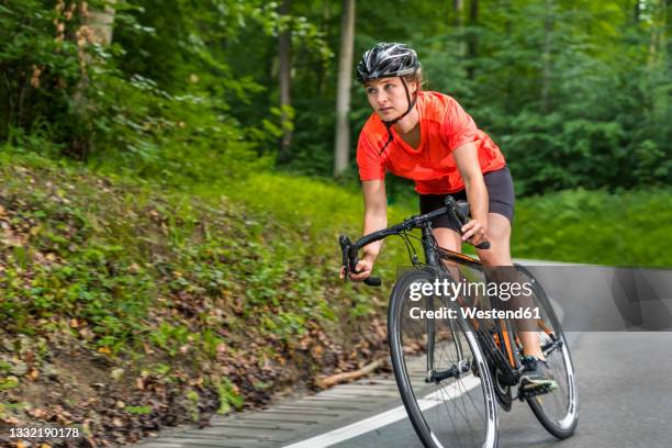 female athlete riding bicycle on road in forest - athleticism stockfoto's en -beelden