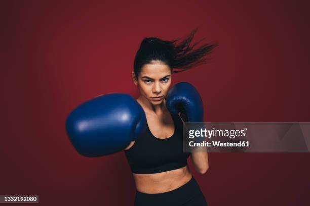 female athlete practicing boxing in front of maroon background - boxing glove coloured background stock pictures, royalty-free photos & images