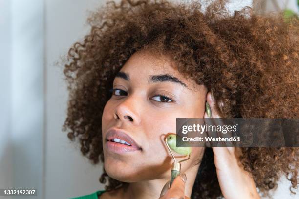 young woman with hand in hair using jade roller on face - facial massage stock pictures, royalty-free photos & images