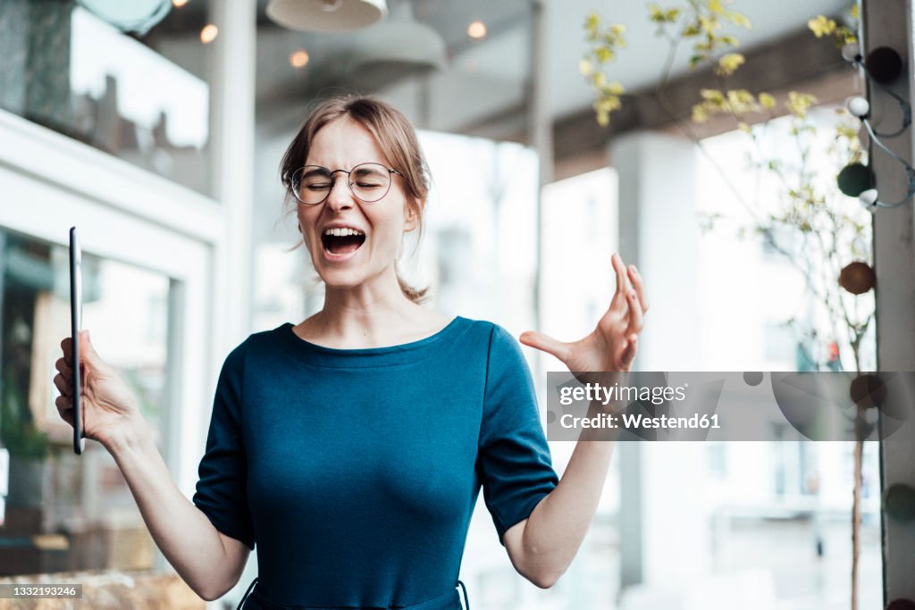 Frustrated businesswoman screaming while holding digital tablet in cafe
