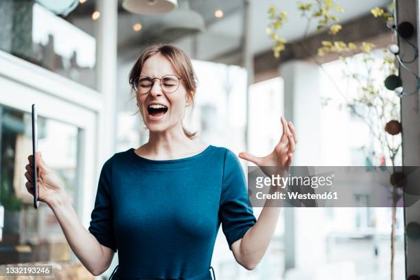 frustrated businesswoman screaming while holding digital tablet in cafe - woedeaanval stockfoto's en -beelden