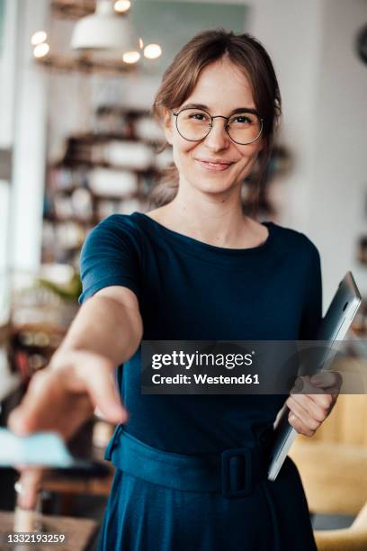 smiling young female freelancer holding laptop giving credit card in cafe - geben stock-fotos und bilder