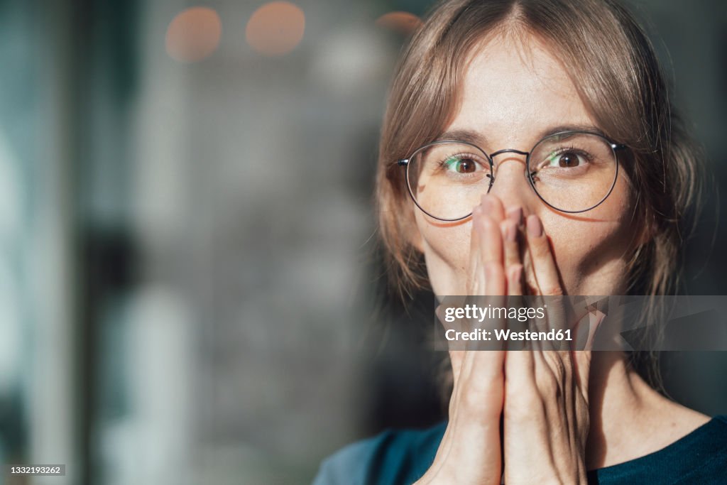 Female professional wearing eyeglasses covering mouth with hands