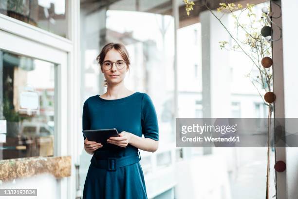 businesswoman holding digital tablet while standing in cafe - dreiviertelansicht stock-fotos und bilder