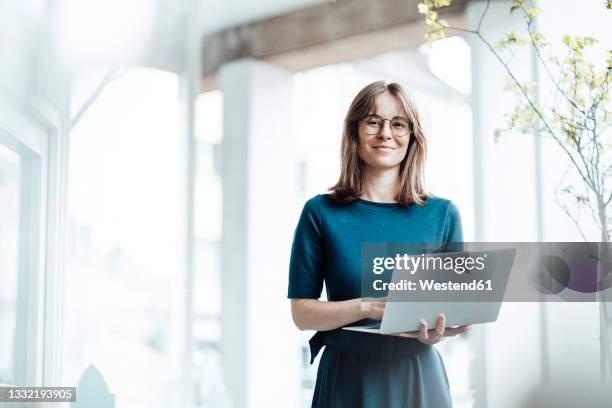 female business professional holding laptop while standing in cafe - standing with laptop imagens e fotografias de stock