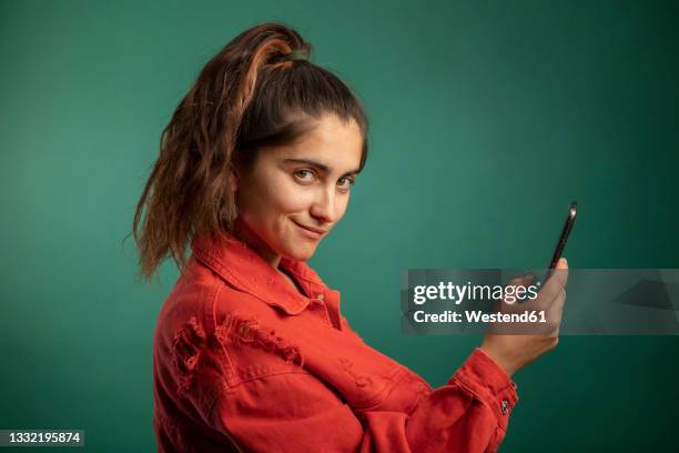 smiling woman holding smart phone - portrait young colour background cool stock-fotos und bilder