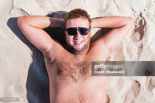 smiling gay man relaxing on sand during sunny day - fat guy on beach fotografías e imágenes de stock