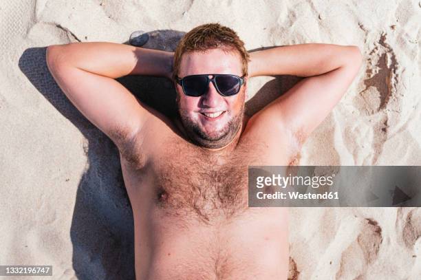 smiling gay man relaxing on sand during sunny day - fat man on beach stockfoto's en -beelden