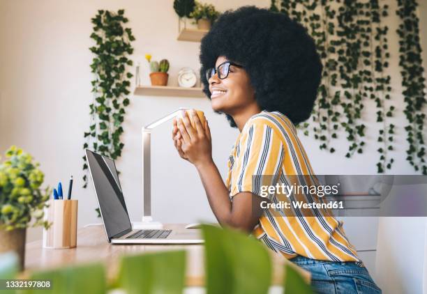 thoughtful young woman sitting with coffee cup at desk at home - table side view stock pictures, royalty-free photos & images