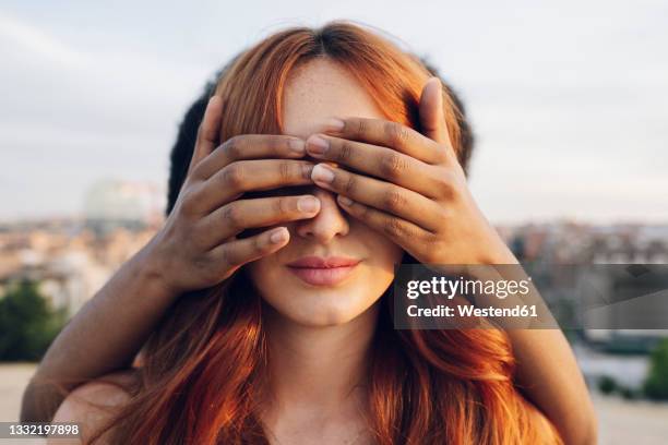 woman covering eyes of redhead girlfriend with hands at sunset - tocan fotografías e imágenes de stock