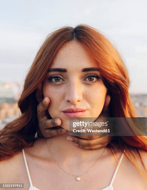 redhead young woman with hands of female friend covering her neck - würgen stock-fotos und bilder