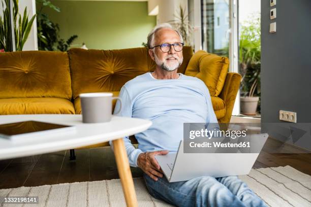 mature man with laptop sitting on floor at home - tisch betrachten stock-fotos und bilder