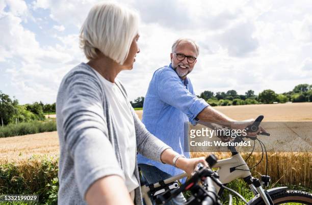 man talking to woman while walking with bicycle on sunny day - 55 59 anni foto e immagini stock
