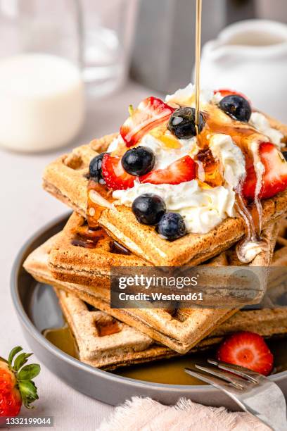maple syrup pouring on stack of fresh waffles with blueberries, strawberries and ice cream - repas servi photos et images de collection