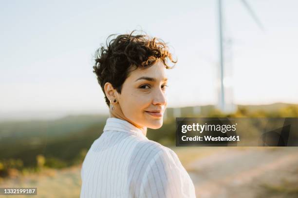 smiling mid adult woman looking over shoulder during sunset - short fotografías e imágenes de stock