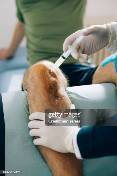 physical therapy: anonymous doctor holding patient leg while giving him injection - knee injection stock pictures, royalty-free photos & images