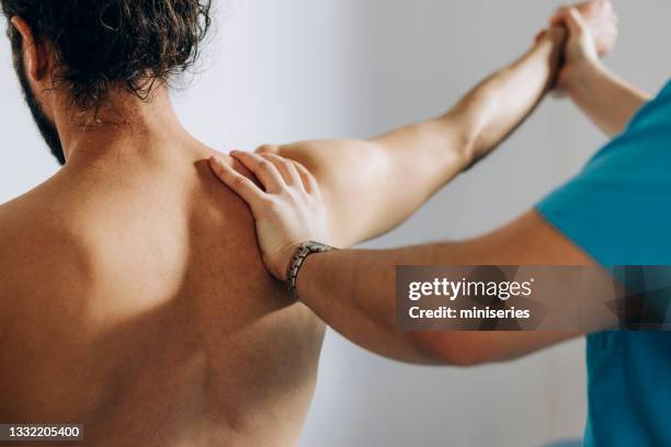 physical therapy: chiropractor doing shoulder adjustment while patient is sitting on the bed - physiotherapy shoulder stock pictures, royalty-free photos & images