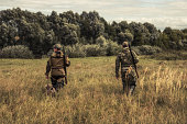 Hunters going through rural field towards forest during hunting season