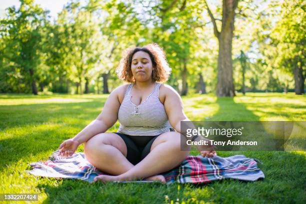 young woman meditating sitting on blanket in park - corp exteriors ahead of earnings figures stockfoto's en -beelden