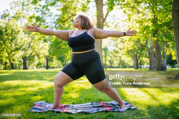 young woman practicing yoga outdoors in park - overweight fotografías e imágenes de stock