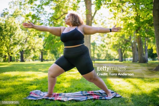 young woman practicing yoga outdoors in park - fat people stock pictures, royalty-free photos & images