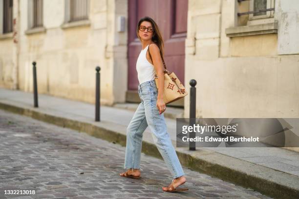 Alexandra Pereira wears brown sunglasses from Tod's, a white ribbed tank top, a beige large wicker bag from Vuitton with printed monograms, pale blue...