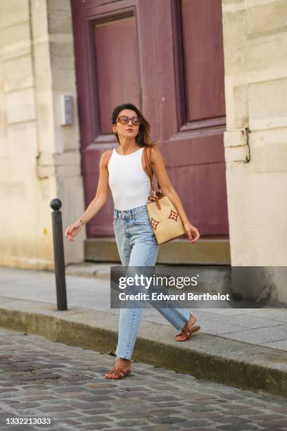 Alexandra Pereira wears brown sunglasses from Tod's, a white ribbed tank top, a beige large wicker bag from Vuitton with printed monograms, pale blue...