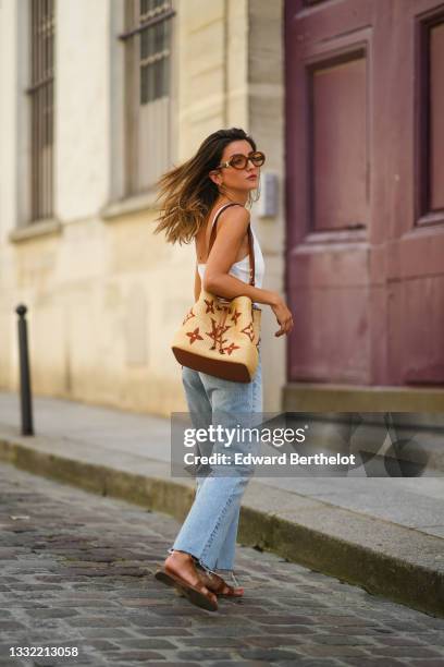 Alexandra Pereira wears brown sunglasses from Tod's, a white ribbed tank top, a beige large wicker bag from Vuitton with printed monograms, pale blue...