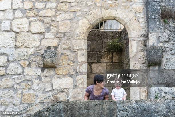 mother looking at her little boy, both of them are smiling. they are crouched on a kerb of a staircase, this staircase takes you to the entrance of a park which you have to pass under a limestone arch. it belonged to an ancient castle. - southern european descent stock pictures, royalty-free photos & images