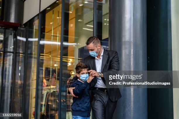 young father and his lovely boy with face masks are standing in the street during a pandemic time. - fashionable dad stock pictures, royalty-free photos & images