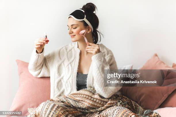 beautiful woman giving herself a face massage with a rose quartz roller and oil at home. - 玉石滾輪 個照片及圖片檔