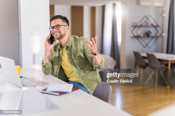 happy young man working at home and talking on phone. - phone interview event stock pictures, royalty-free photos & images