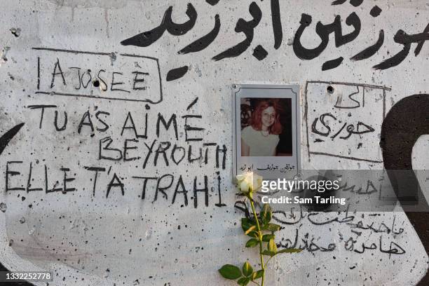 Fresh white rose stands by a photograph of blast victim Josephine Abou Zeid, by the walls of Beirut Port, on August 4, 2021 in Beirut, Lebanon....