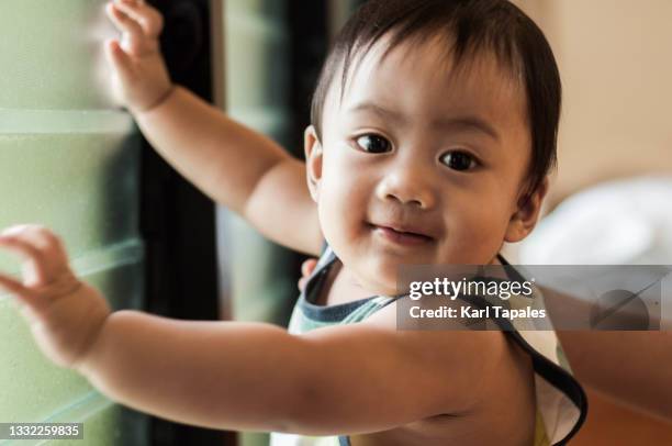 candid portrait of a southeast asian baby boy learning to walk at home - daily life in philippines stockfoto's en -beelden