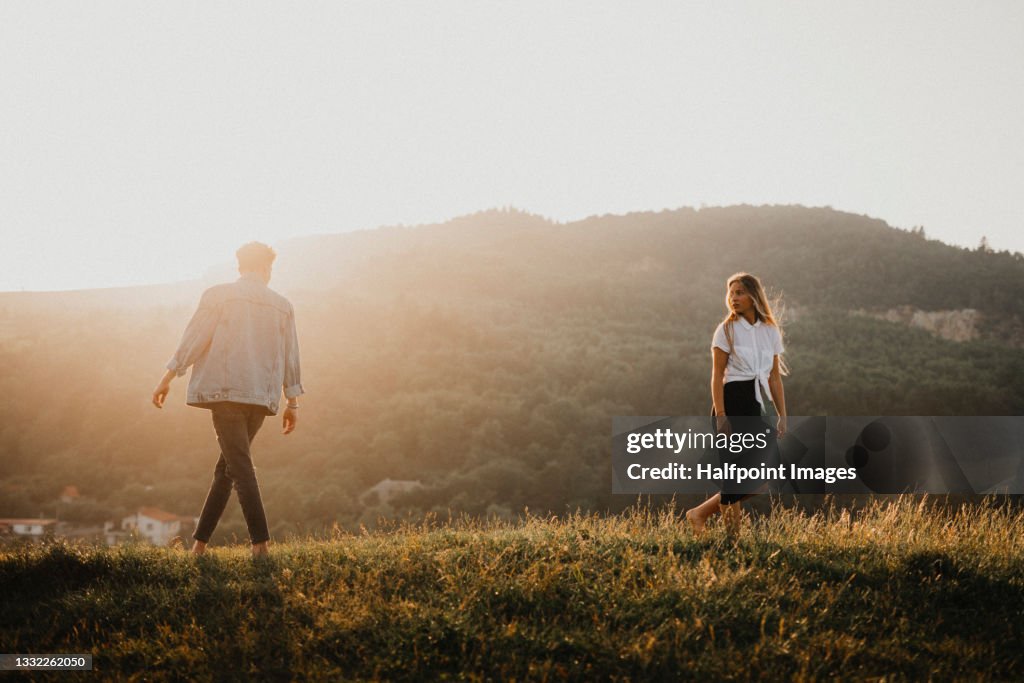 Portrait of young couple on a walk outdoors in nature, walking away from each other.