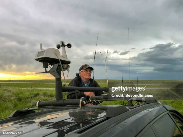 senior storm-chaser checking the horizon for severe storm action after adjusting rooftop tech on his vehicle - caçador de tempestades imagens e fotografias de stock