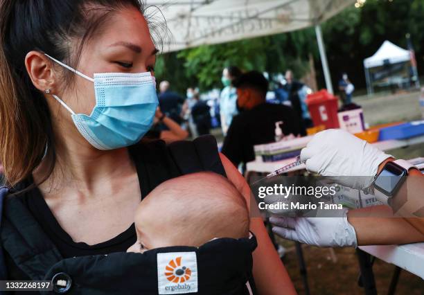 Person receives a COVID-19 vaccination dose, while carrying a baby in tow, as part of a National Night Out event hosted by Melrose Action on August...
