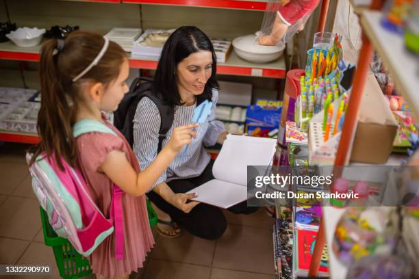 caring mother helping her daughter to choose and buy all the essential school supplies - woman picking up toys stock pictures, royalty-free photos & images